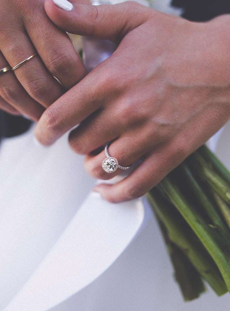 Gros plan sur la bague de fiançailles de la mariée, ses mains posées sur le bouquet