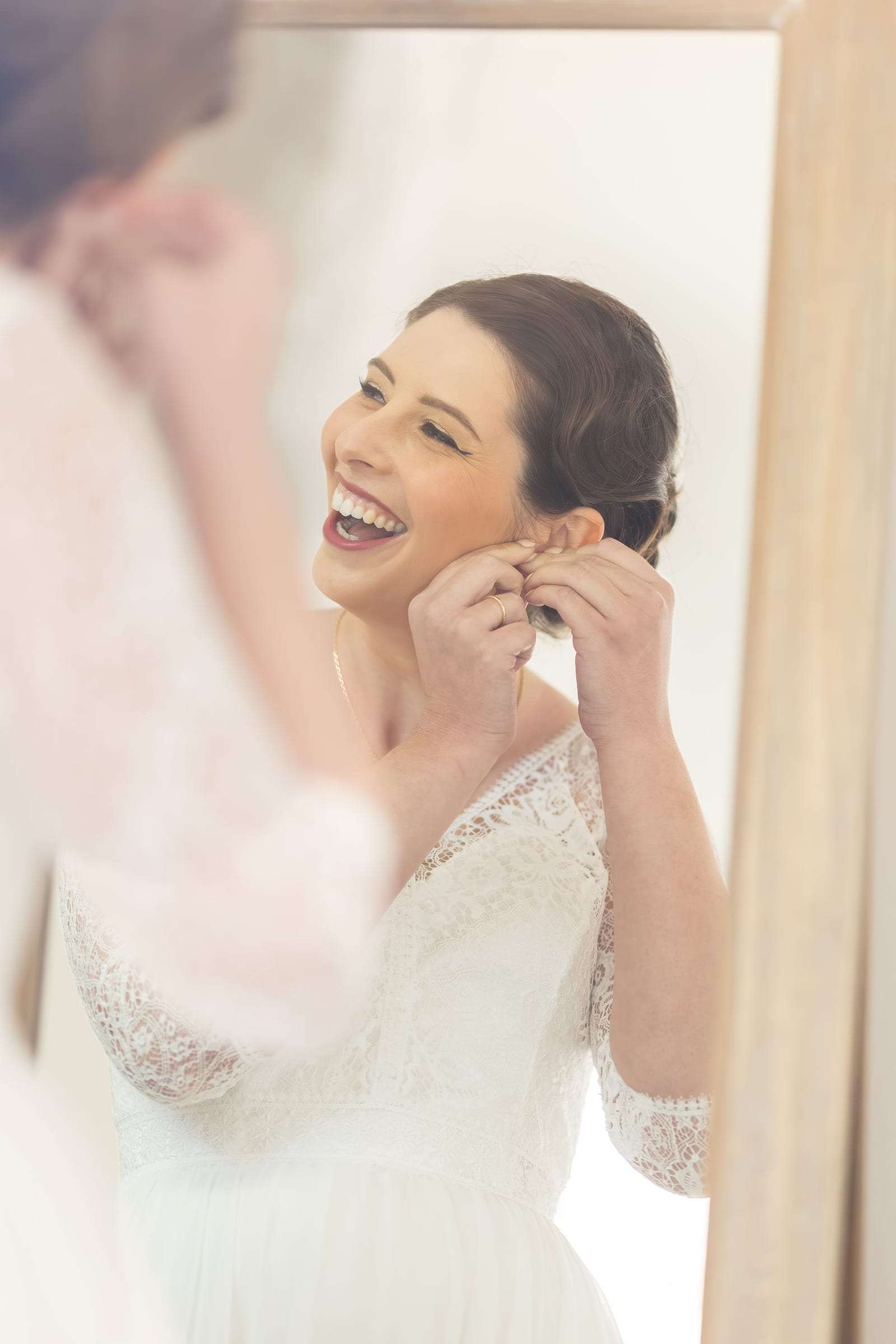 La mariée rit devant le miroir en mettant ses boucles d'oreilles